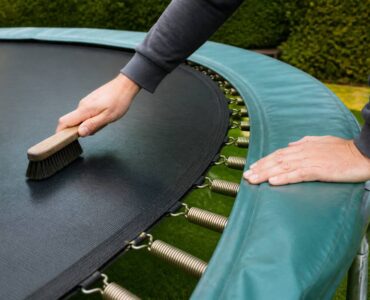 Iemand maakt een trampoline schoon en controleert het frame en de springmat