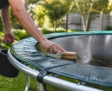 Persoon reinigt springmat en randkussen van een trampoline met een zachte borstel